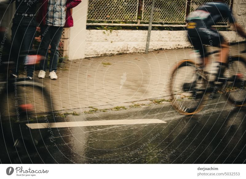 Ein spannendes Radrennen durch die Stadt. Die Radfahrer fliegen fast vorbei. Ein paar Zuschauer betrachten dies von einem Hauseingang. Farbfoto Straße