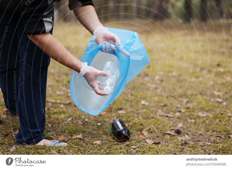 Eine Frau mit Handschuhen sammelt gebrauchte Plastikflaschen ein und steckt sie in einen blauen Müllsack. Ein Freiwilliger säubert den Park an einem sonnigen, hellen Tag. Aufräumen, Verschmutzung, Ökologie und Plastikkonzept