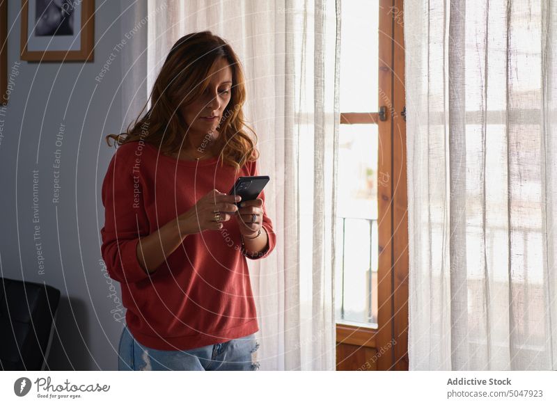 Reife Frau sendet eine Textnachricht Lächeln Nachricht Smartphone Fenster benutzend Browsen senden Glück heimwärts Lebensmitte reif hispanisch ethnisch Internet