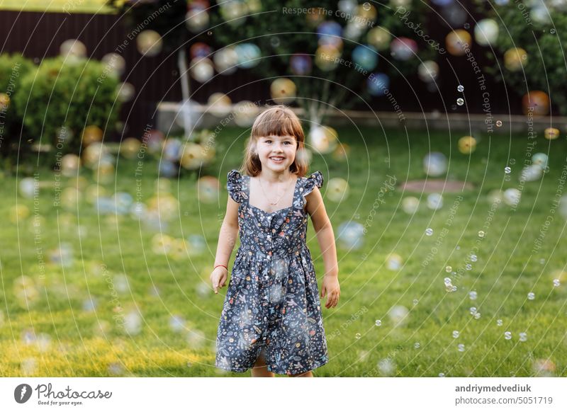 lächelnd Kind Mädchen genießen das Spielen mit Seifenblasen im Freien auf Sommertag. Nettes Kind Kind fängt Seifenblasen in der Natur. glückliche Kindheit Konzept