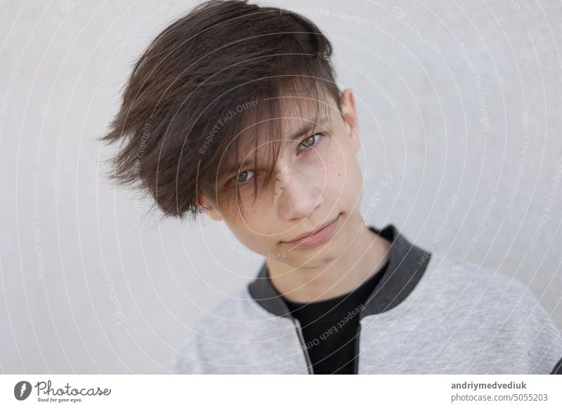 Schöner junger Mann mit stilvollem Haarschnitt. Porträt von Teenager-Junge mit Jugendfrisur steht auf grauem Hintergrund und schaut in die Kamera. Gesicht