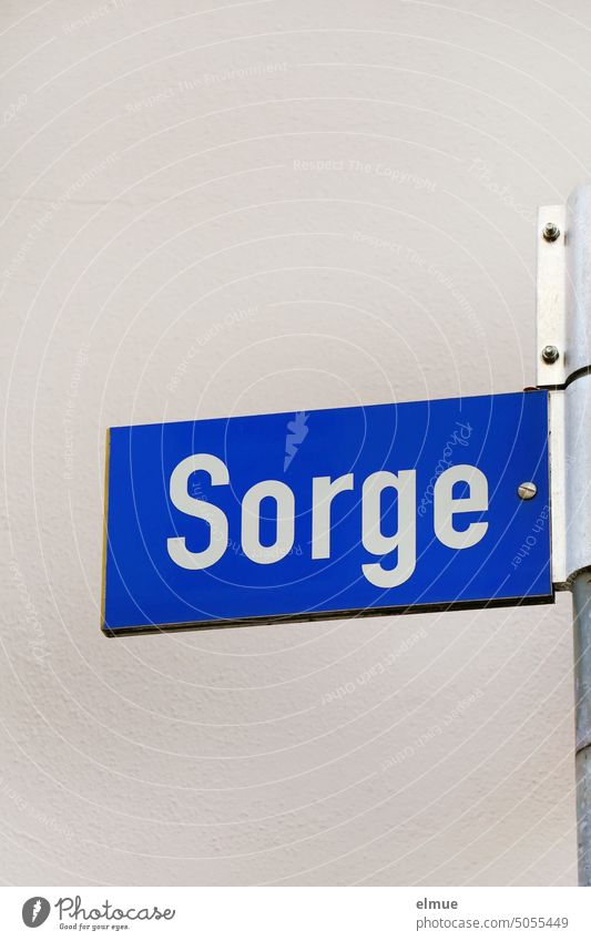 blaues Straßennamenschild - Sorge - an einer Metallstange vor einer hellen Wand Sorgen Straßenschild Orientierung Adresse wohnen Schilder & Markierungen