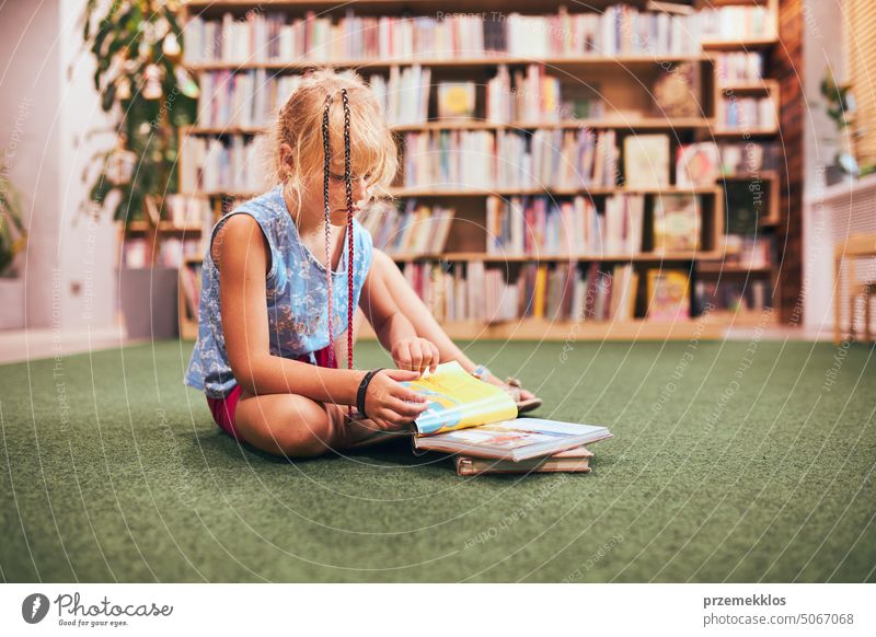 Schulmädchen, das in der Schulbibliothek ein Buch liest und beobachtet. Erledigt Hausaufgaben. Bücher in Regalen in einer Buchhandlung. Aus Büchern lernen. Zurück zur Schule