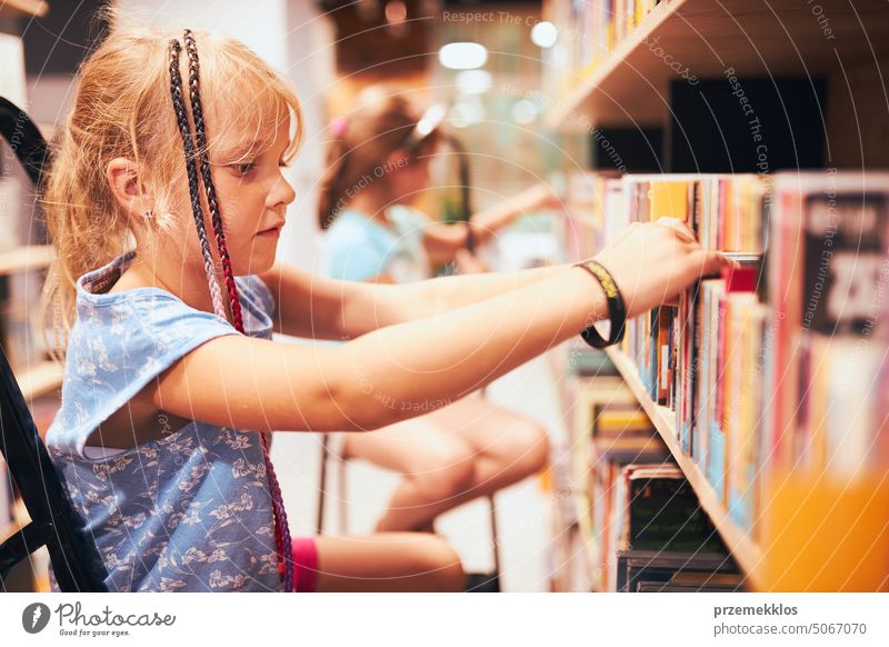 Schülerinnen suchen in der Schulbibliothek nach Büchern. Schüler wählen Bücher aus. Grundschulbildung. Erledigung der Hausaufgaben. Zurück zur Schule Rücken