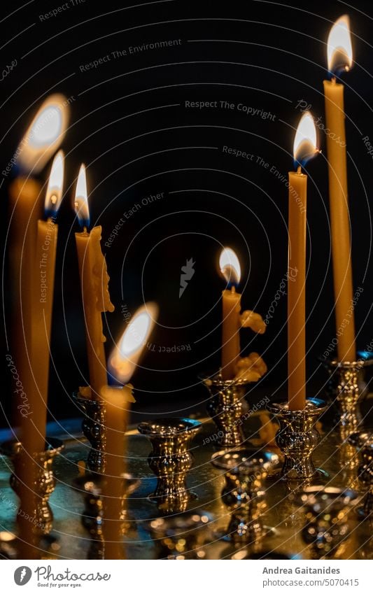 Sieben lange dünne brennende orangefarbene Opferkerzen Gedenkkerzen in goldenen Kerzenhaltern stehend, vertikal, schwarzer Hintergrund Lichter Kiche Glaube