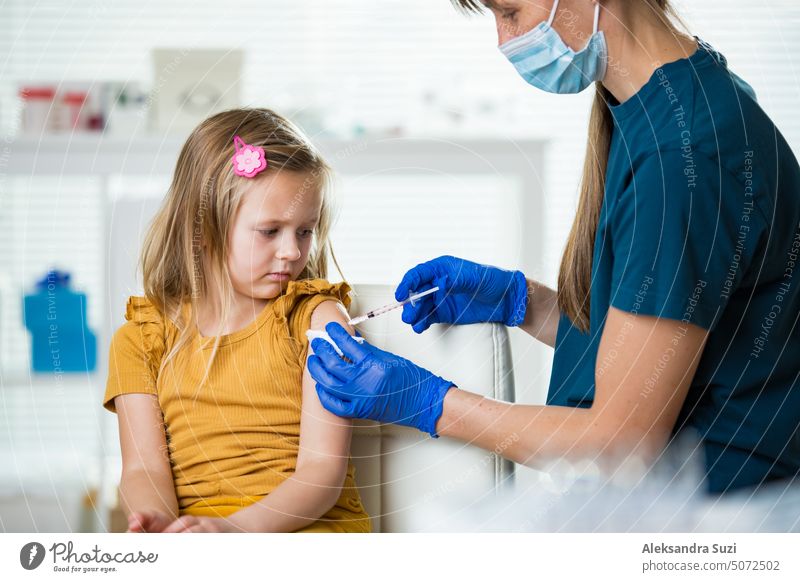 Weibliche Krankenschwester mit chirurgischer Maske und in Handschuhen gibt einem Kind in der Klinik eine Impfstoffinjektion. Kinderimpfung. Antibiotikum