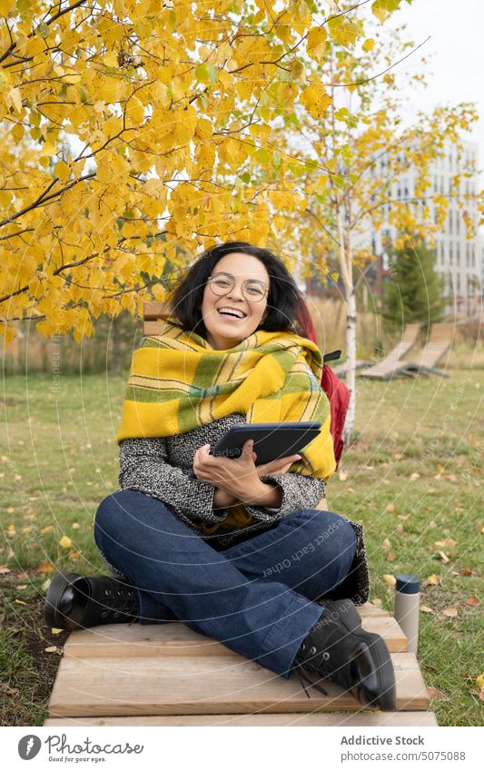 Fröhliche Frau mit Tablet-PC im Park freiberuflich Tablette digital benutzend Herbst Bank Decke Browsen Apparatur Glück Gerät heiter soziale Netzwerke jung