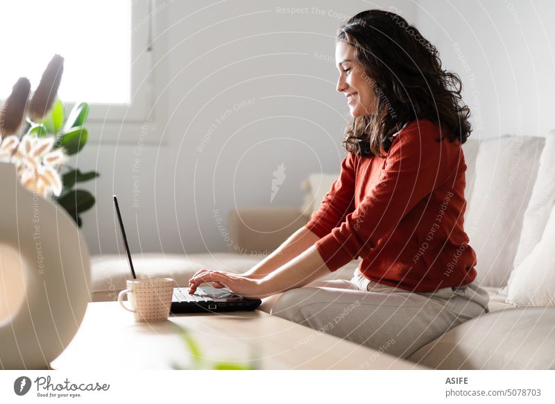 Glückliche junge Frau mit Laptop auf der Couch sitzend heimwärts Liege Lächeln online Internet Technik & Technologie schön arbeiten Sitzen Computer Business