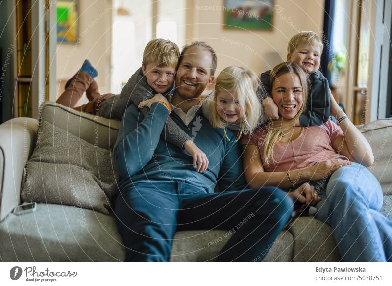 Glückliche junge Familie sitzt zu Hause auf dem Sofa reales Leben echte Menschen Bonden im Innenbereich qualitätsvolle Zeit Kindererziehung Genuss Zusammensein