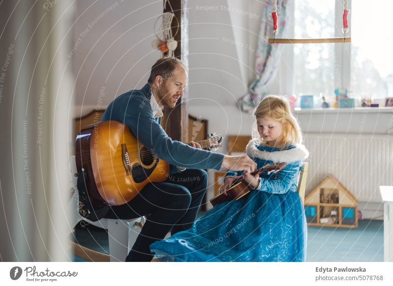 Vater bringt seiner Tochter das Gitarrespielen bei moderne Männlichkeit genderblend reales Leben echte Menschen Bonden Familie im Innenbereich