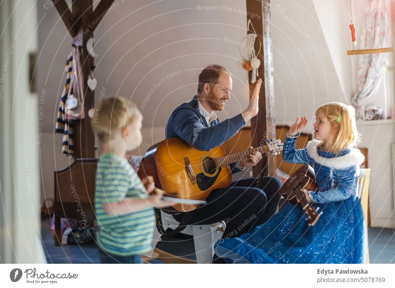 Papa bringt seinen Kindern das Gitarrespielen bei moderne Männlichkeit genderblend reales Leben echte Menschen Bonden Familie im Innenbereich