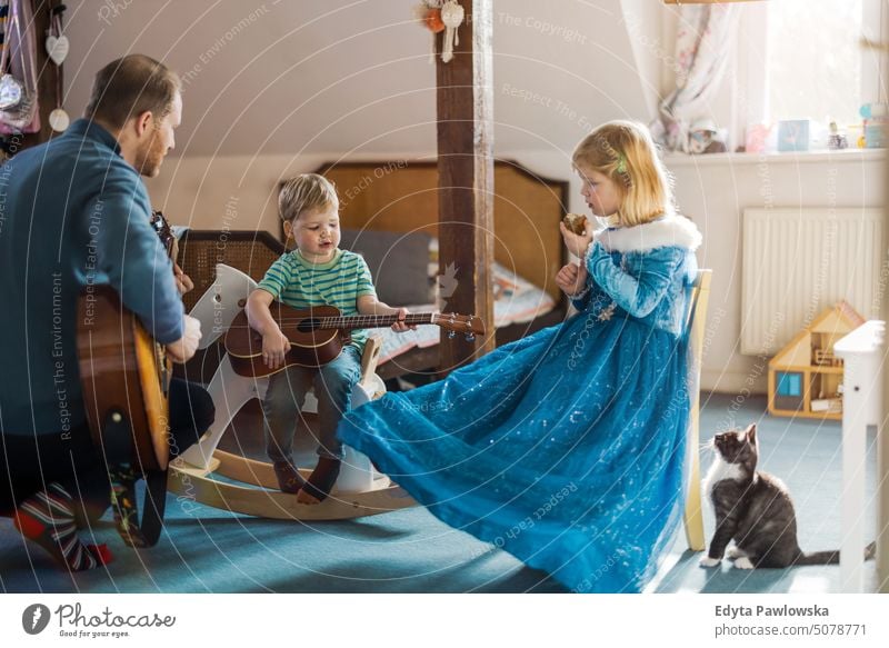 Papa bringt seinen Kindern das Gitarrespielen bei moderne Männlichkeit genderblend reales Leben echte Menschen Bonden Familie im Innenbereich
