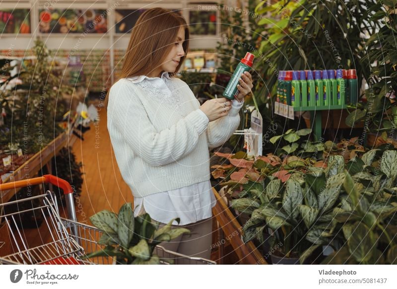 Junge Gärtnerin kauft Pflanzenpflegeprodukte in einem Blumenladen in Innenräumen. Frau Flasche Garten Produkt Pflege Werkstatt Halt Blätter Tonic Laden Spray