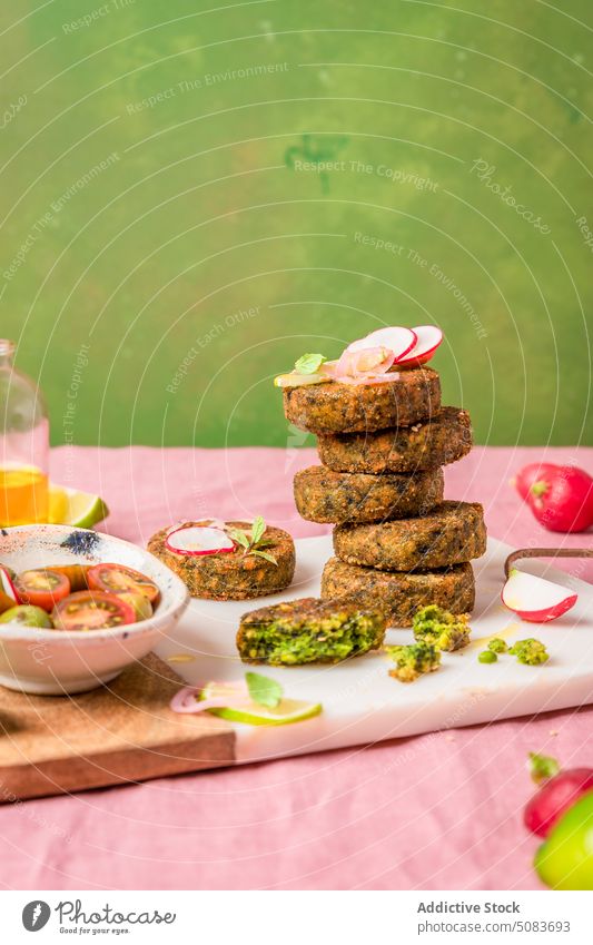 Vegetarische Krapfen, serviert auf einem Schneidebrett neben einer Schale mit Kirschtomaten drücken Kalk Fritter Stapel Vegetarier frisch Tomate dienen