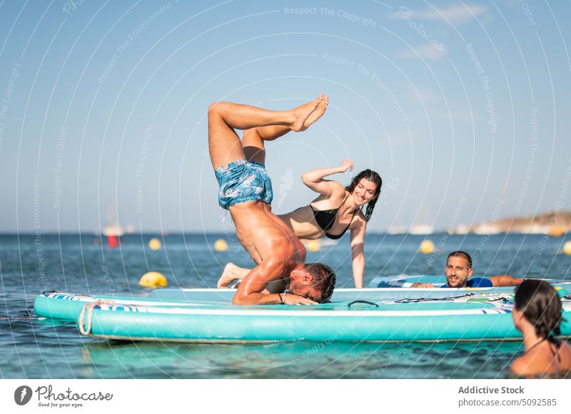 Gut gelaunte Freunde beobachten einen Mann, der einen Kopfstand auf einem Paddelbrett macht Menschen heiter Zusatzplatine Yoga Glück abstützen MEER Sommer Hobby