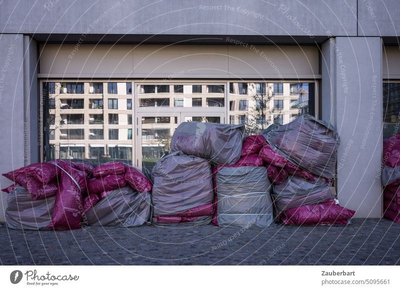 Müllsäcke stapeln sich vor einer Scheibe, in der sich ein modernes Wohngebäude spiegelt spiegeln Spiegelung Fassade Wohnhaus Stadt städtisch urban Widerspruch