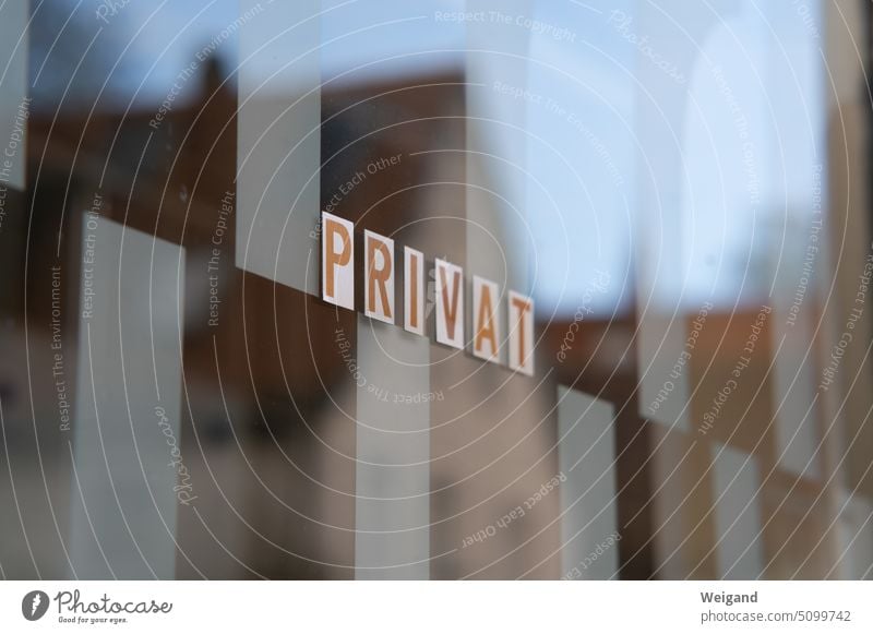 Detailaufnahme Fensterscheibe, in der sich ein gegenüberliegendes Haus spiegelt und auf der einzelne Buchstaben-Sticker kleben, die das Wort PRIVAT lesen lassen