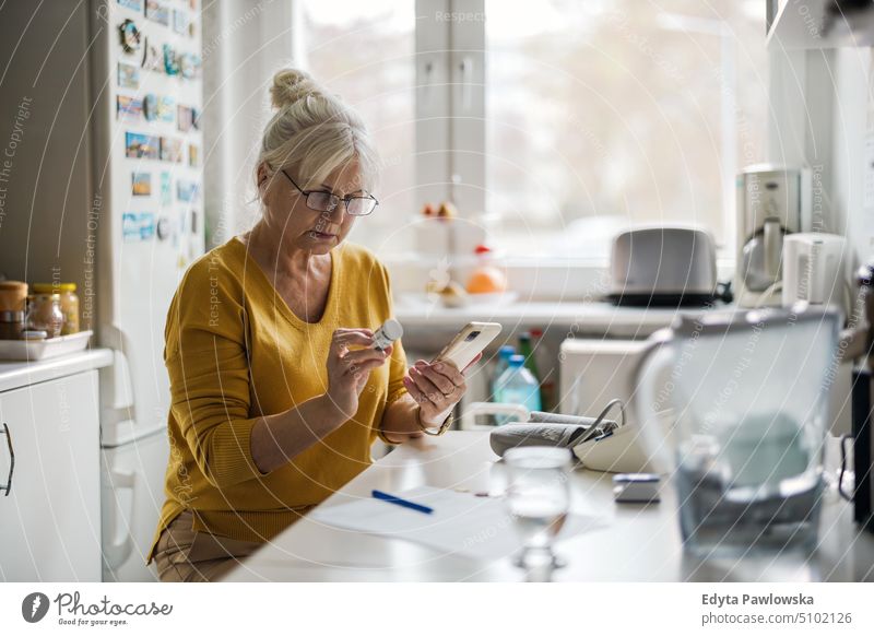 Ältere Frau prüft Rezept mit Mobiltelefon Menschen Senior reif älter heimwärts Haus alt Alterung häusliches Leben Großmutter Rentnerin in den Ruhestand getreten