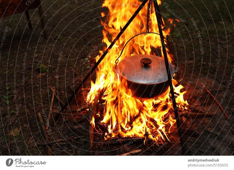 Kochen im Freien unter Feldbedingungen. Ein Kessel auf einem Feuer im Wald. Kochen auf dem Scheiterhaufen auf Reisen. Dreibein mit Melone auf einem Feuer beim Picknick. Konzeptuelles Reisen, Trekking und Abenteuer