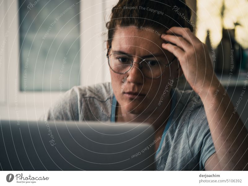Junge Frau mit Brille  sitzt vor einem PC und greift sich mit den Fingern an den Kopf. pc Computer Bildschirm Arbeit heimwärts Internet Technik & Technologie