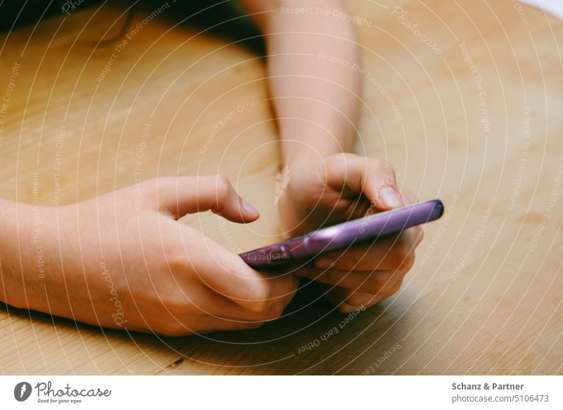 Hände einer jungen Person halten violett farbenes Smartphone. Die Arme sind auf einer Hölzernen Tischplatte abgelegt. Chatten Pubertät 13-18 Jahre Jugendliche