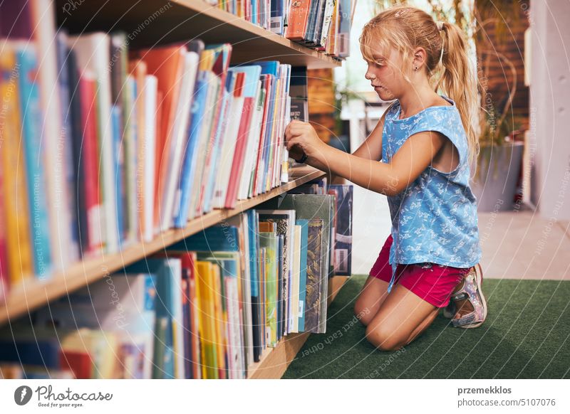 Schülerin auf der Suche nach einem Buch zum Lesen in der Schulbibliothek. Schülerin wählt Literatur zum Lesen aus. Bücher in Regalen in einer Buchhandlung. Lernen aus Büchern. Zurück zur Schule