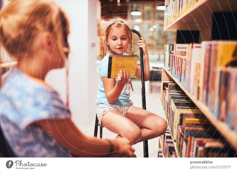 Schülerinnen suchen in der Schulbibliothek nach Hörbüchern. Schüler wählen Bücher aus. Grundschulbildung. Erledigung der Hausaufgaben. Zurück zur Schule Rücken