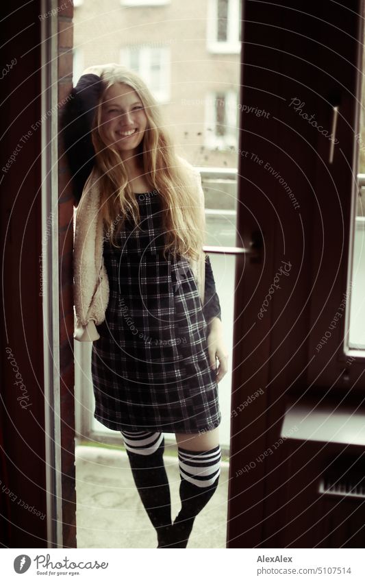 Portrait durch die Balkontür einer jungen blonden Frau in Kleid und Strümpfen junge Frau Sessel Beine Kniestrümpfe lächeln Freude Gelassenheit zuhause