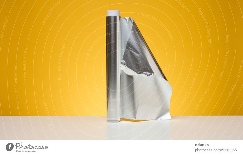 Rolle gedrehter Lebensmittelfolie zur Verpackung von Lebensmitteln auf gelbem Hintergrund Folie gefaltet rollen blättern Schot Glanz Aluminium Leichtmetall