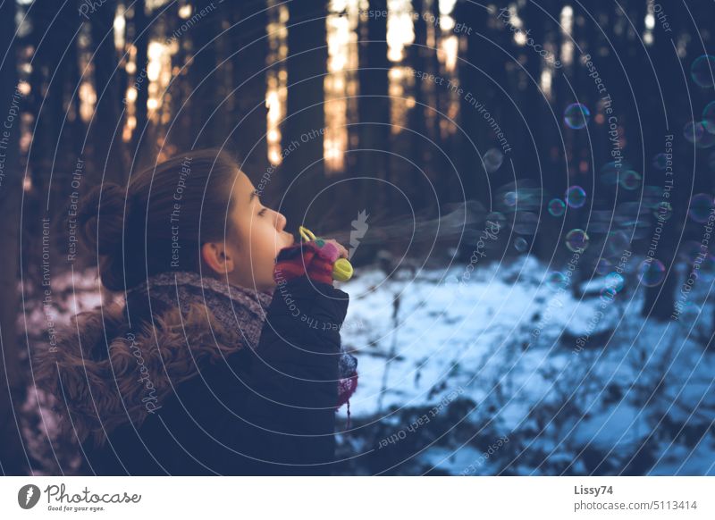 Mädchen, das im Winter-Wald Seifenblasen pustet Kind Kindheit Spass Freude pusten Schnee Kindheitserinnerung Abendsonne Bäume Aufenaufnahme Farbfoto