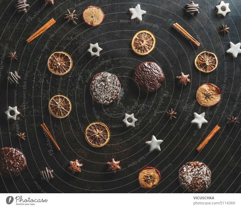Weihnachten Muster mit getrockneten Orangen, Zimtstangen, Lebkuchen und Weihnachtsplätzchen auf dunklen Küchentisch Hintergrund gemacht. Ansicht von oben.