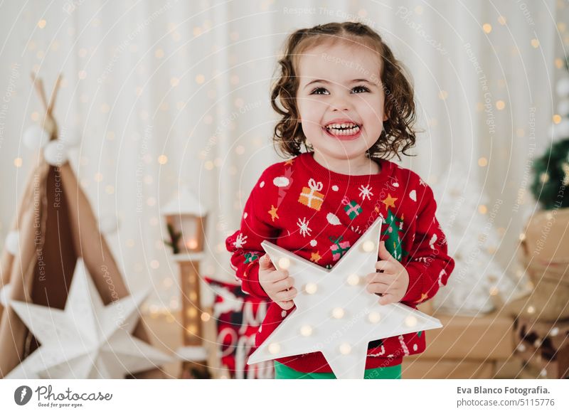 Lächelndes kleines Mädchen zu Hause mit einem Stern in der Hand zur Weihnachtszeit Kind Weihnachten heimwärts Geschenke Glück heiter niedlich 2 Kinder Familie