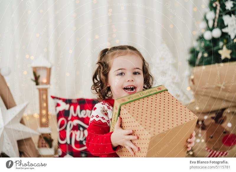 Fröhliches kleines Mädchen zu Hause in der Weihnachtszeit mit einem Geschenkkarton Kind Weihnachten heimwärts Geschenke Glück heiter niedlich 2 Kinder Familie