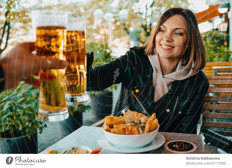 Glückliche Frau stößt mit einem Mann in einem asiatischen Café in Deutschland mit Biergläsern an. Positive Dame während Oktoberfest Feier. Alkohol Glas jung
