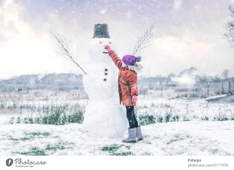 Kleines Mädchen fügt eine Karotte für die Nase des Schneemanns hinzu Sonnenuntergang Frost jung purpur Kaukasier Lifestyle Frau frostig Freizeit Kinder Hut