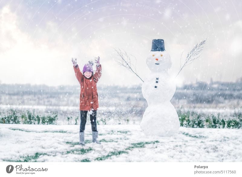 Mädchen jubelt mit einem Schneemann im Schnee Sonnenuntergang Frost jung purpur Kaukasier Lifestyle Frau frostig Freizeit Kinder Hut Schneefall Winterzeit