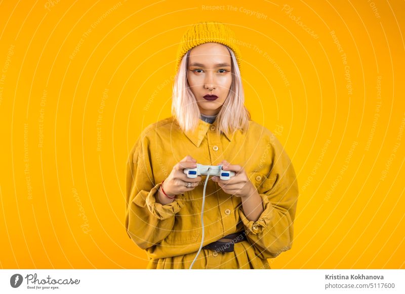 Hübsches junges Mädchen spielt Video spannendes Spiel auf Tv mit Joystick auf gelbe Studio Wand. Mit moderner Technologie. Spaß im Innenbereich Spielen Konsole