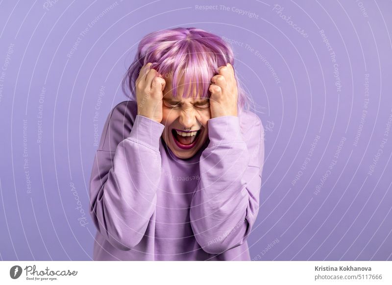 Verängstigte und schreiende Frau mit gefärbtem lila Haar schockiert isoliert über violettem Hintergrund. Gestresst und deprimiert hübsches Mädchen wegen der schlechten Nachrichten.