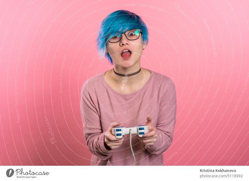 Hübsches junges Mädchen mit blauer Frisur spielen Video spannende Spiel auf Tv mit Joystick auf rosa Studio Wand. Mit moderner Technologie. Spaß im Innenbereich