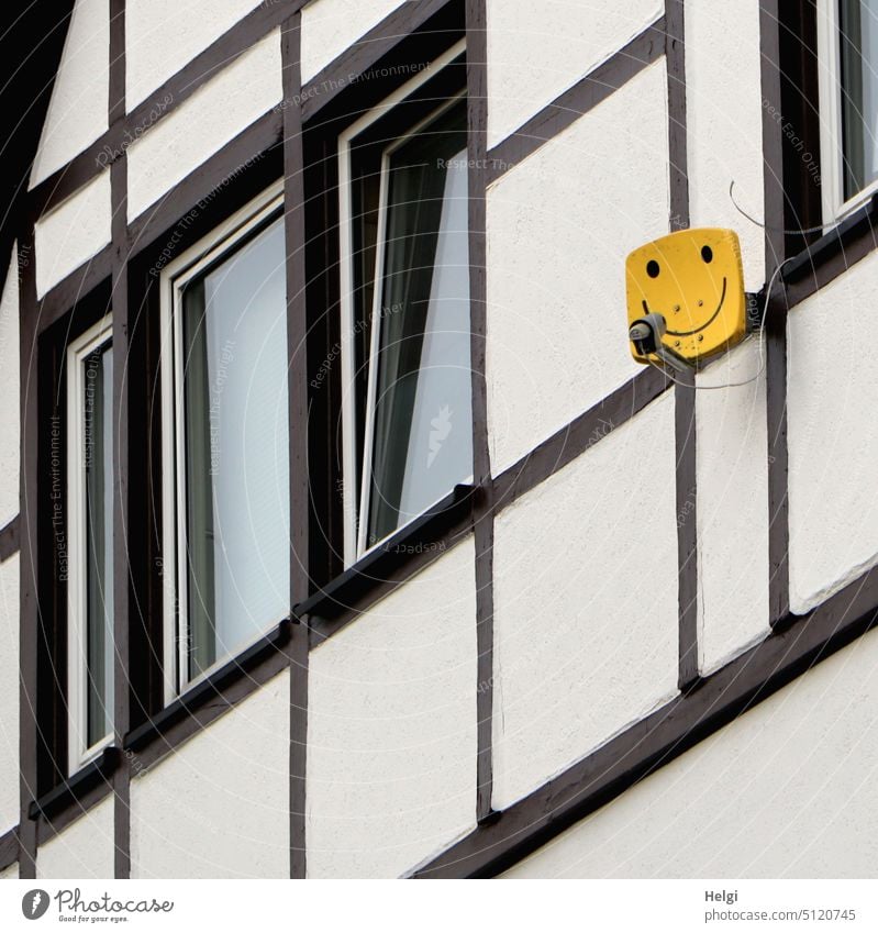 Satellitenschüssel in Form eines gelben Smileys  an der Wand eines Fachwerkhauses Antenne Empfang Haus Gebäude Fassade Fenster Lächen außergewöhnlich weiß