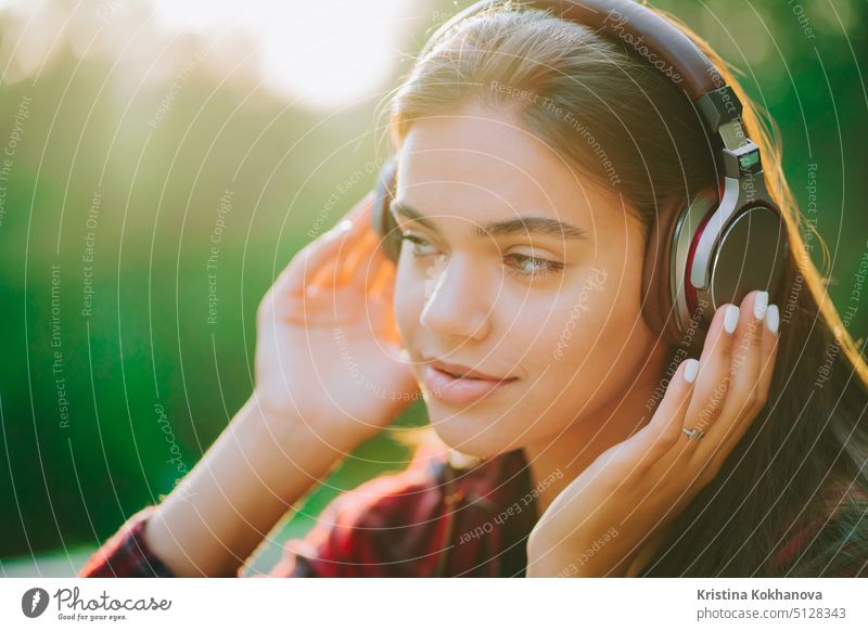 Nettes Mädchengesicht mit Kopfhörern. Junge Frau genießt Musik, während sie im grünen Park sitzt. Konzept der Jugend, Freiheit, Technologie Person im Freien