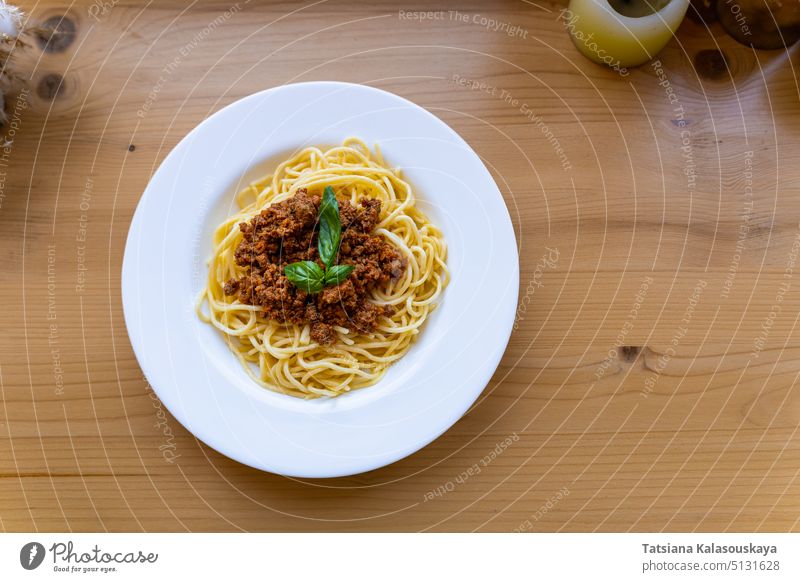 Spaghetti Bolognese in weißem Teller, dekoriert mit Basilikumblatt auf Holztisch, Ansicht von oben. Klassisches Gericht der italienischen Küche. Blatt hölzern