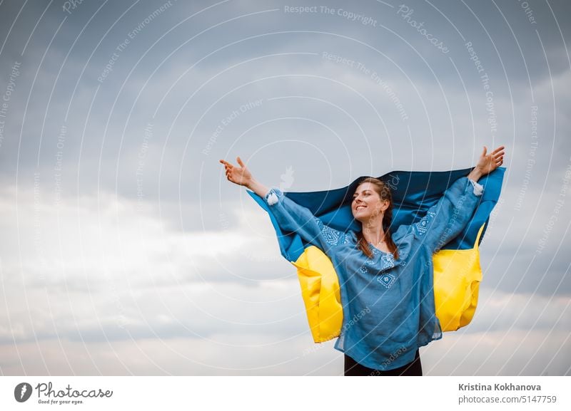 Lächelnde ukrainische Frau mit Nationalflagge auf Himmel Hintergrund. Porträt der jungen Dame in blauer Stickerei vyshyvanka. Kopieren Raum. Ukraine, Unabhängigkeit, Freiheit, patriotisches Symbol, Sieg im Krieg.