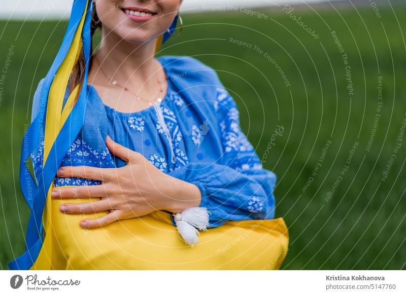 Lächelnde ukrainische Frau mit Nationalflagge auf grünem Feld Hintergrund. Junge Dame in blauer Stickerei vyshyvanka. Ukraine, Unabhängigkeit, Freiheit, patriotisches Symbol, Sieg im Krieg.