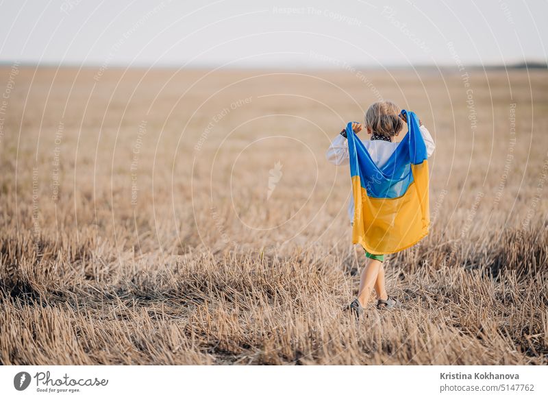Glücklicher kleiner Junge - ukrainischer Patriot Kind mit Nationalflagge im Feld nach der Sammlung Weizen, offene Fläche. Ukraine, Frieden, Unabhängigkeit, Freiheit, Sieg im Krieg.