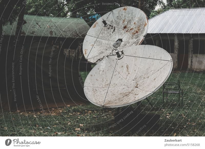 Antennenschüsseln stehen neben Zelt und vor mit Wellblech gedeckten Häusern in düsterer Stimmung Empfang Video Satellit Satellitenempfang Satellitenschüssel