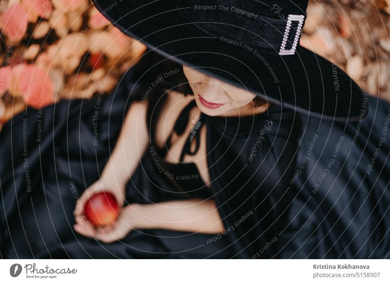 Porträt einer Frau als Hexe in Schwarz mit einem roten Apfel als Symbol der Versuchung Wut Kunst Herbst Hintergrund schön Schönheit bizarr schwarz Feier Kind