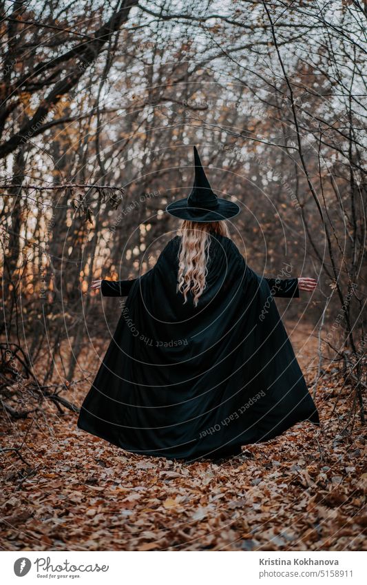 Blonde Hexe in langem schwarzem Umhang und Hut auf herbstlichem Waldhintergrund. Halloween Mädchen Entsetzen spukhaft Person Frau dunkel Kind Tracht