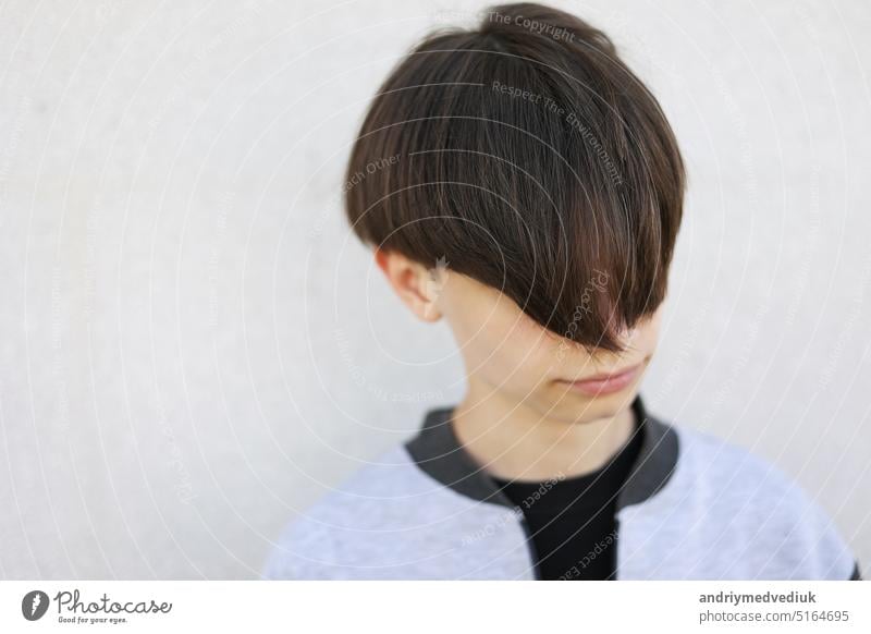 Schöner junger Mann mit stilvollem Haarschnitt. Porträt von Teenager-Junge mit Jugendfrisur steht auf grauem Hintergrund. Gesicht gutaussehend Lifestyle Frisur