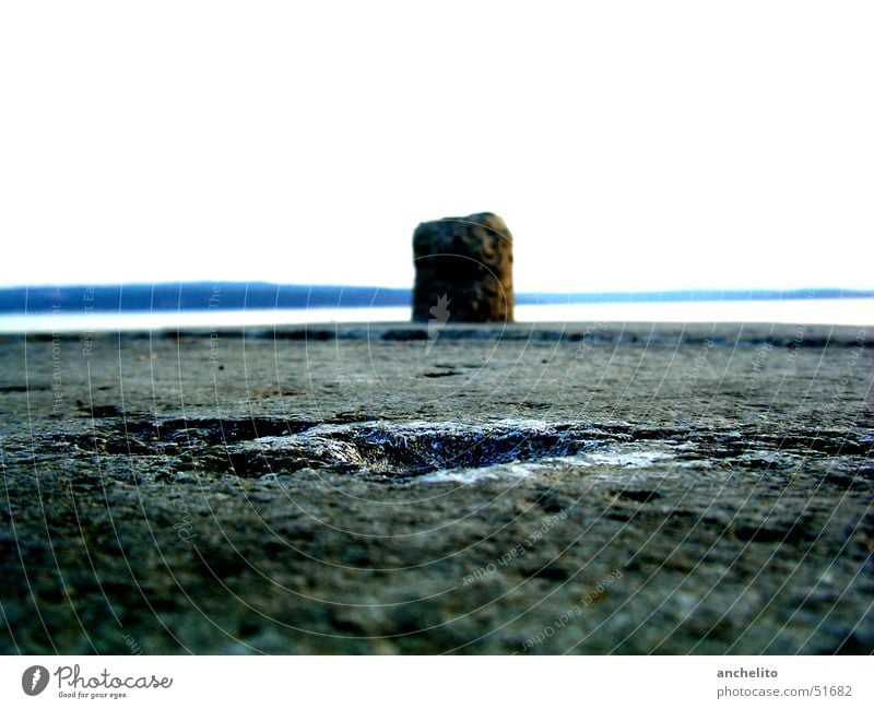 einsamer Poller vor der weiten See Asphalt Meer grau Himmel weiß Einsamkeit Ferne Befestigung Strand Küste pollard Stein stone Bodenbelag tarmac coarse ocean